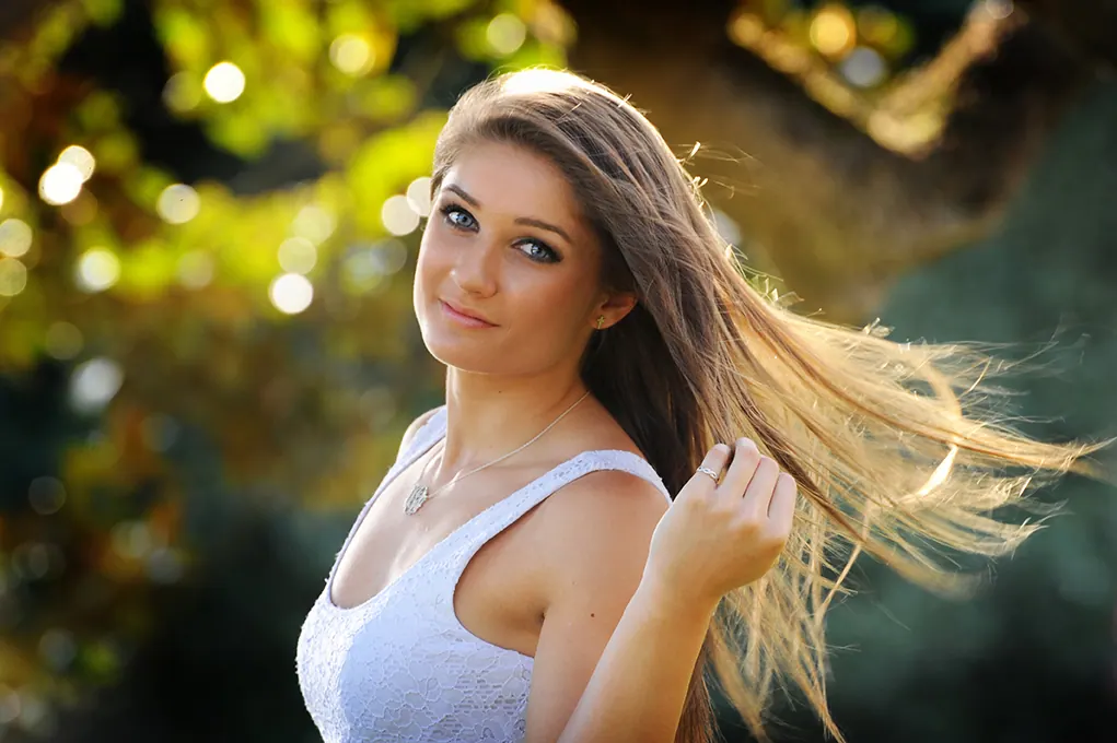 Senior girl with windswept hair in warm golden backlight under oak trees