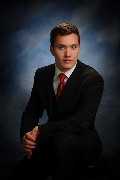 Classic studio senior portrait of a young man in a black suit and red tie