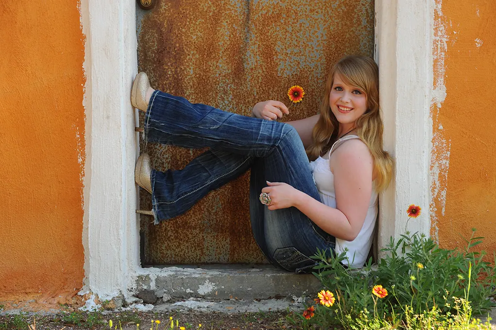 Senior girl with a sunflower sitting in an orange stucco doorway
