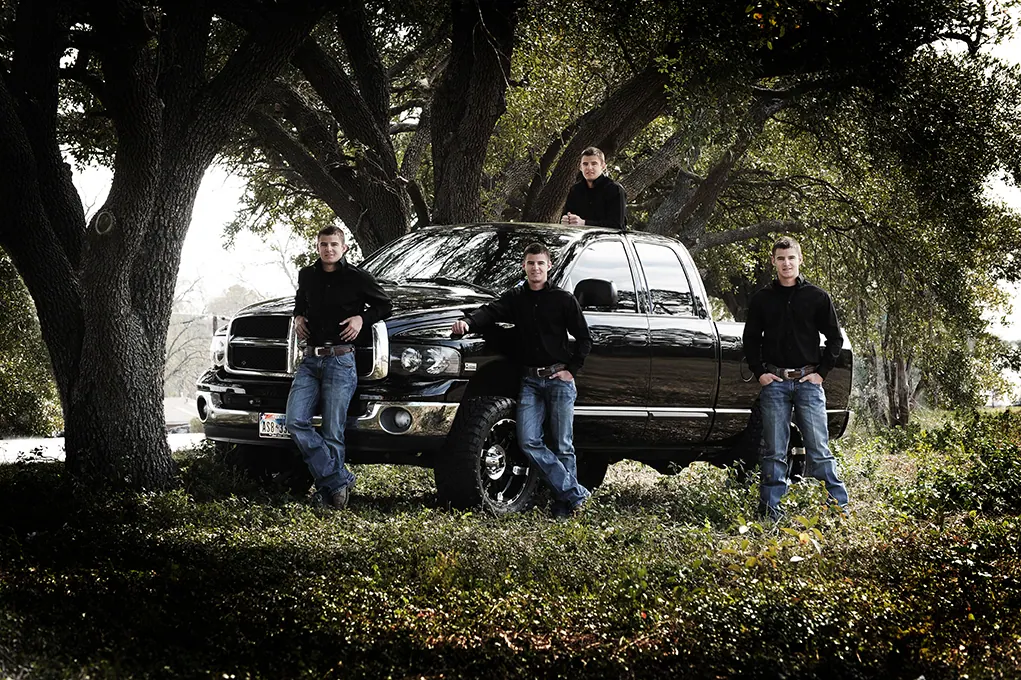 Three seniors with a black pickup truck under live oak trees