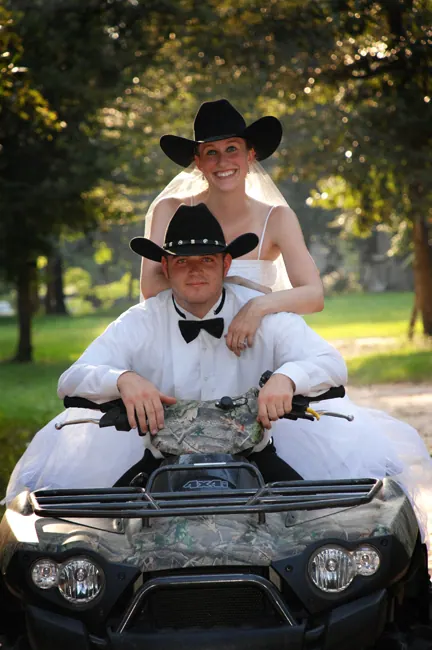 Bride and groom in cowboy hats riding a camouflage ATV