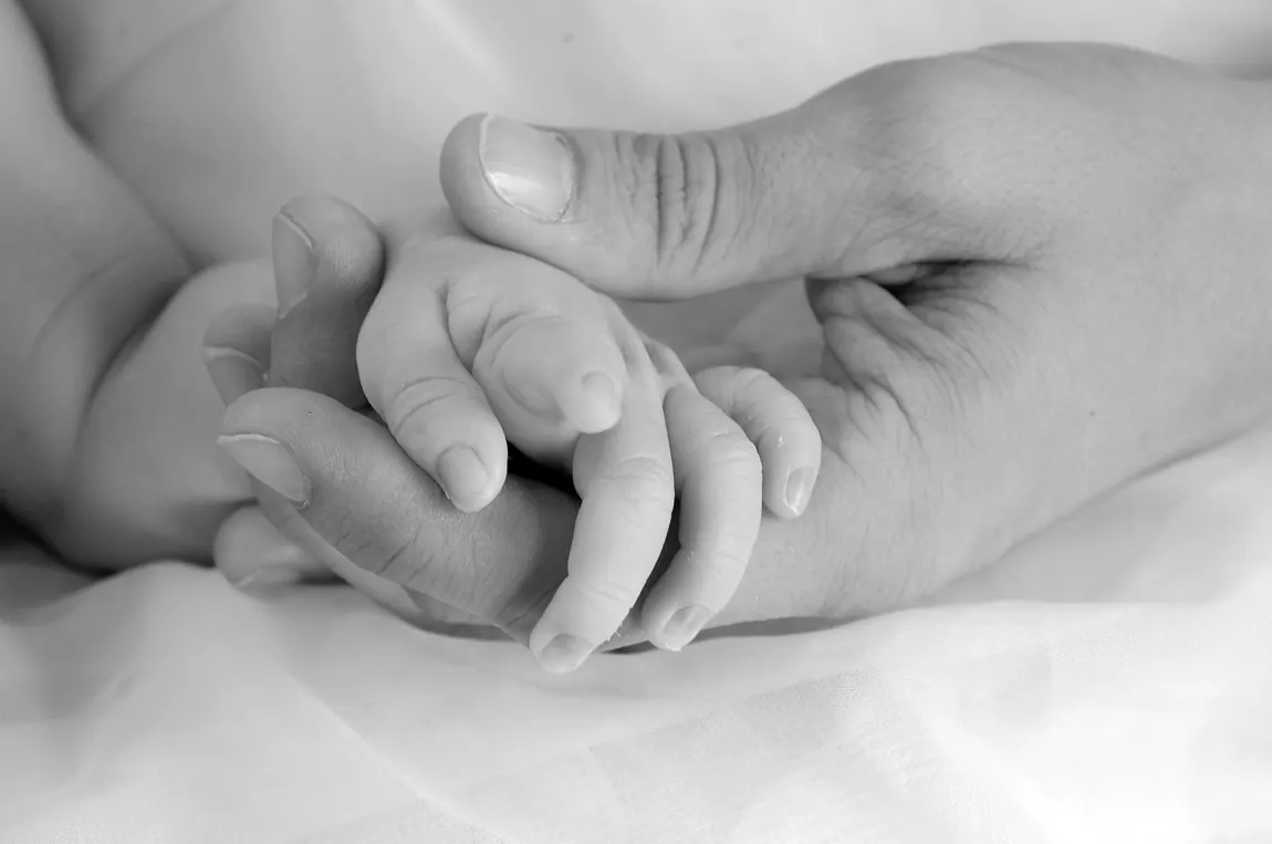 Black-and-white close-up of a baby's hand holding a parent's finger