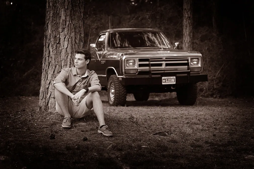 Sepia portrait of a senior sitting in front of his vintage pickup truck in the pines