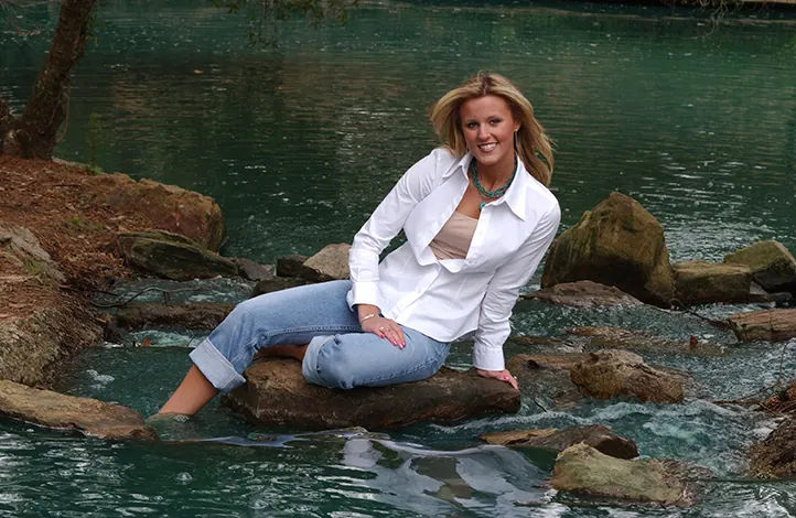 Senior girl in a white shirt sitting on rocks in a green river