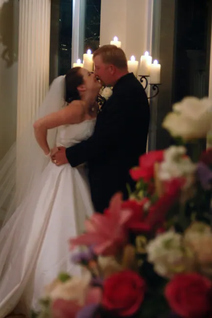 Bride and groom kissing in candlelight behind roses
