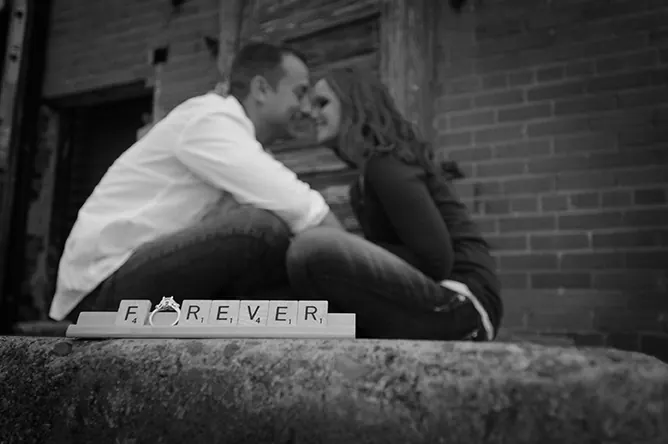 Black-and-white engagement portrait of a couple with a FOREVER sign