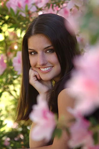 Smiling brunette senior framed by pink azalea blossoms