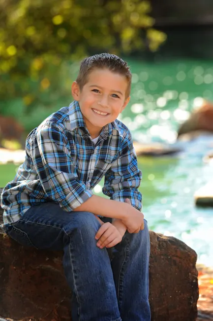 Smiling boy in a plaid shirt sitting on a rock by a creek