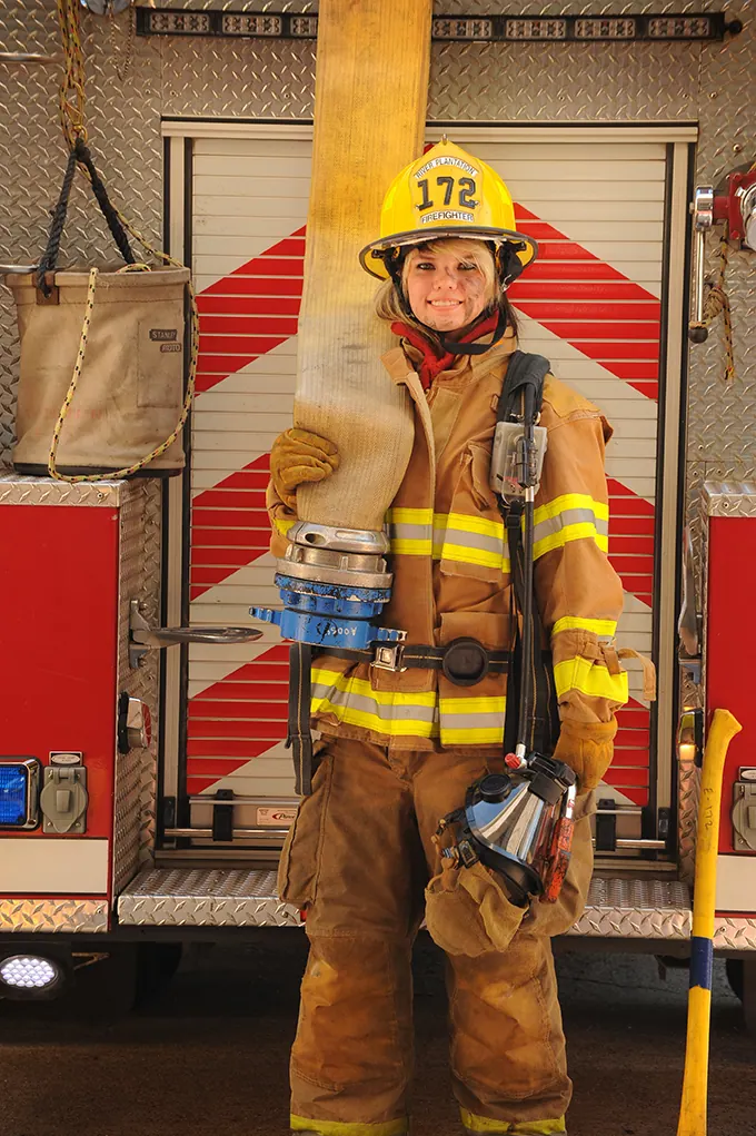 Senior in full firefighter turnout gear standing in front of a fire engine