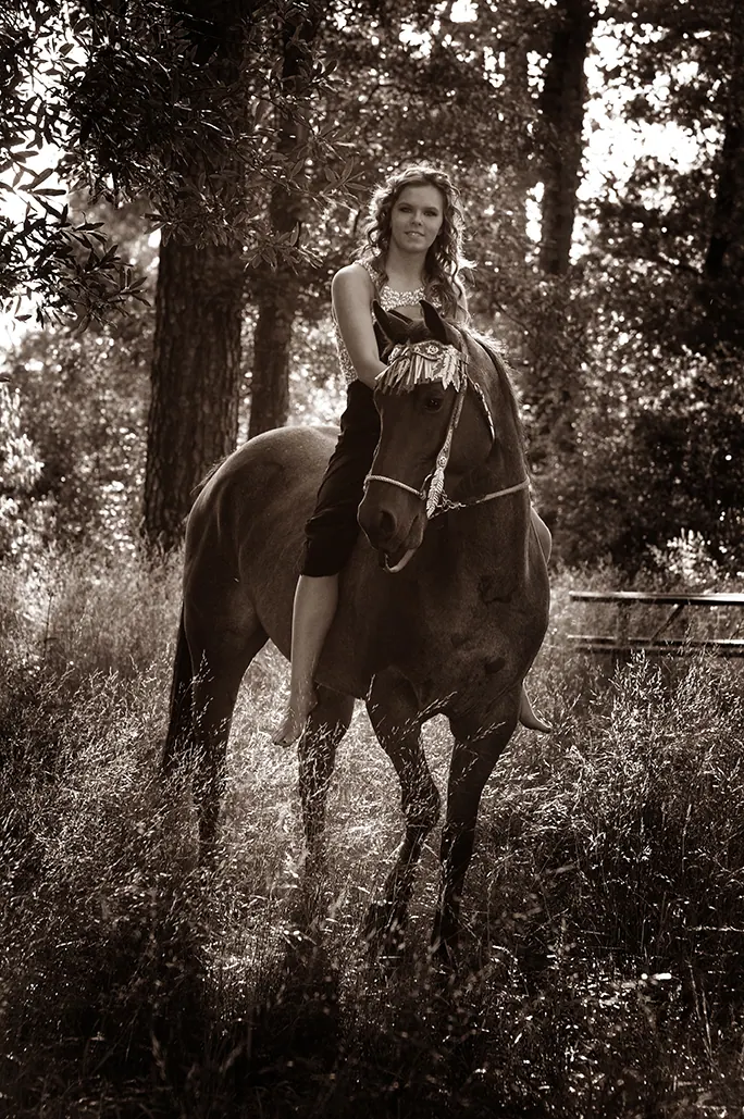 Sepia portrait of a senior girl riding her horse through tall grass