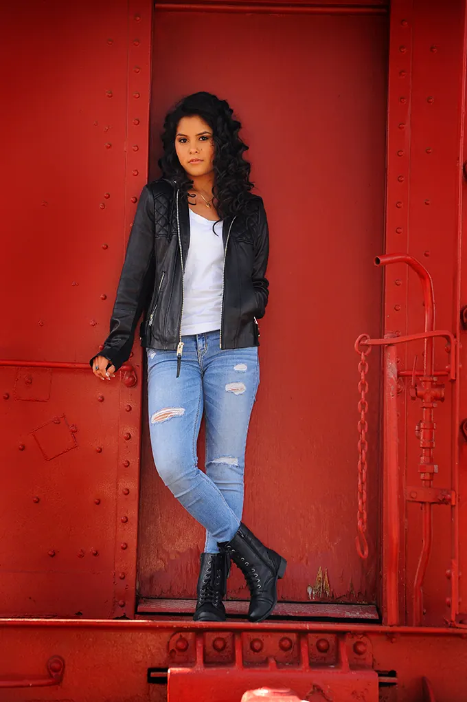 Senior girl in a leather jacket standing in the doorway of a red caboose