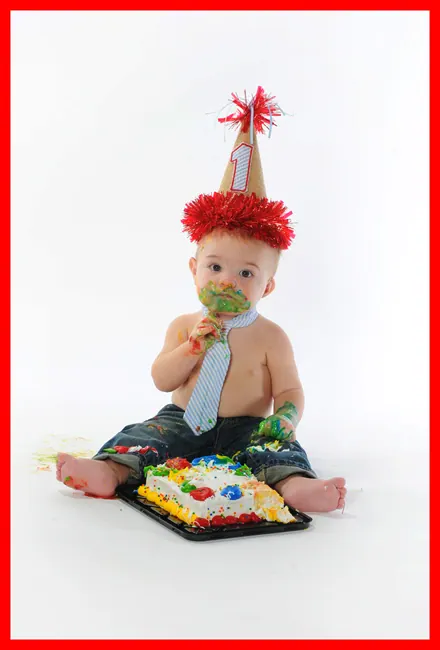 Baby boy in a party hat and tie smashing his first-birthday cake