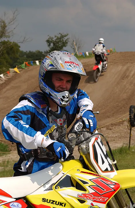 Motocross senior in racing gear sitting on his yellow dirt bike at the track