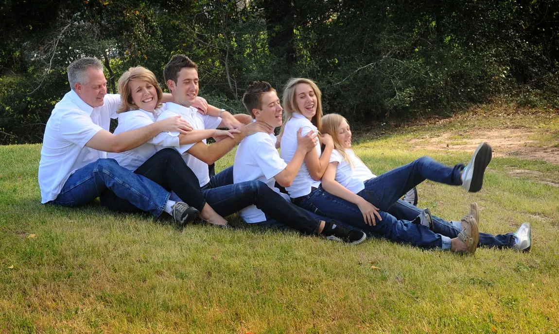 Family in white shirts and jeans lying in a row on a grassy slope