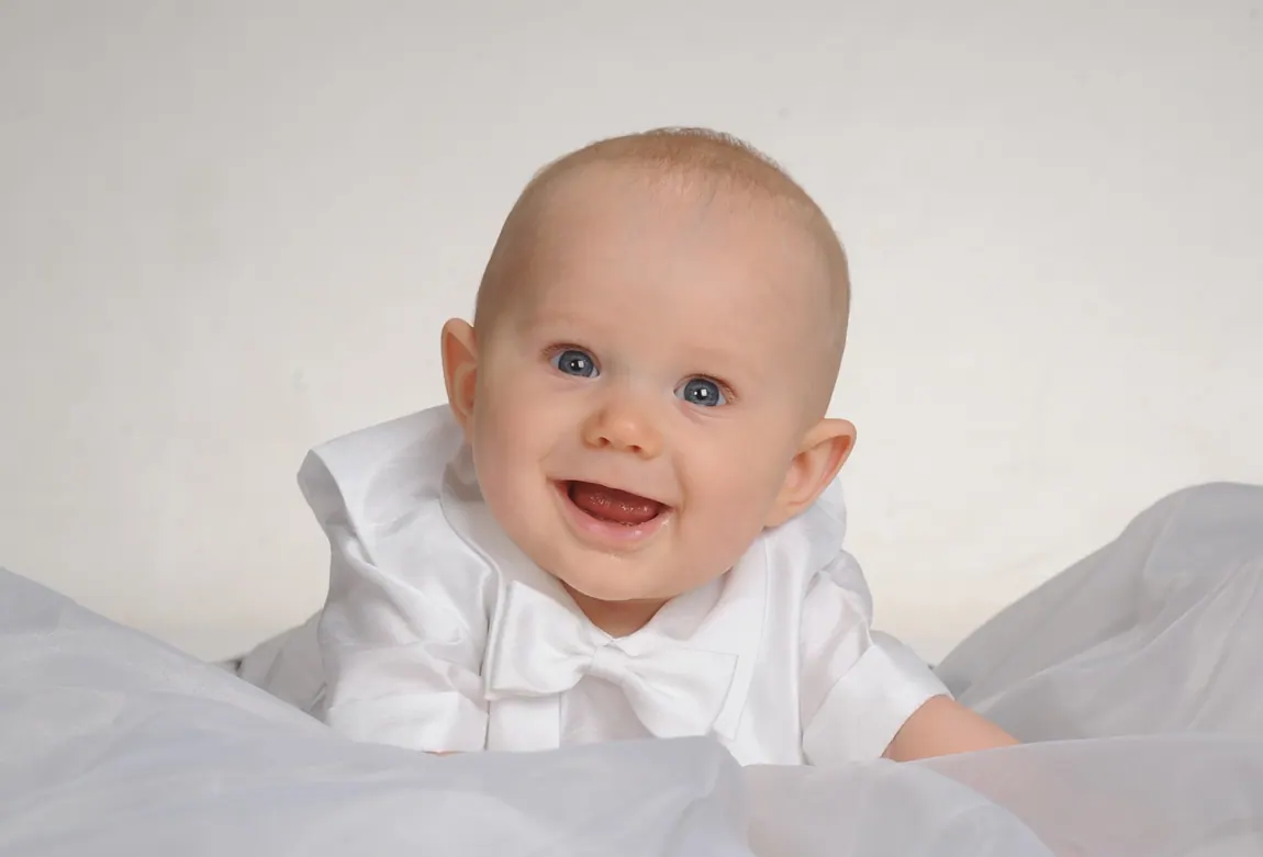 Smiling baby boy in white lying on a white blanket