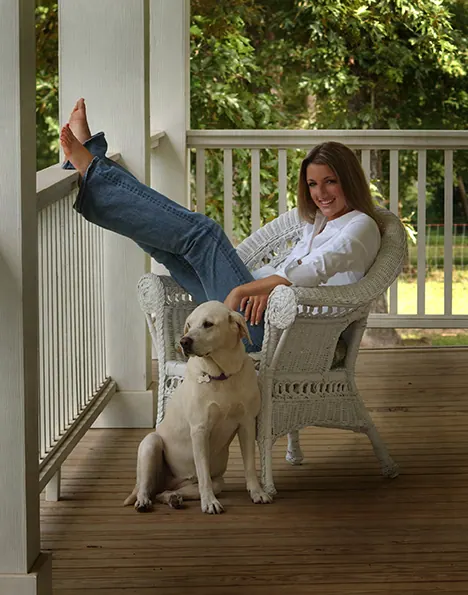 Senior girl relaxing in a wicker chair on a porch with her white dog