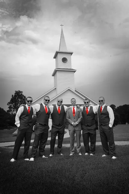 Black-and-white groomsmen with red ties in front of a white steeple church