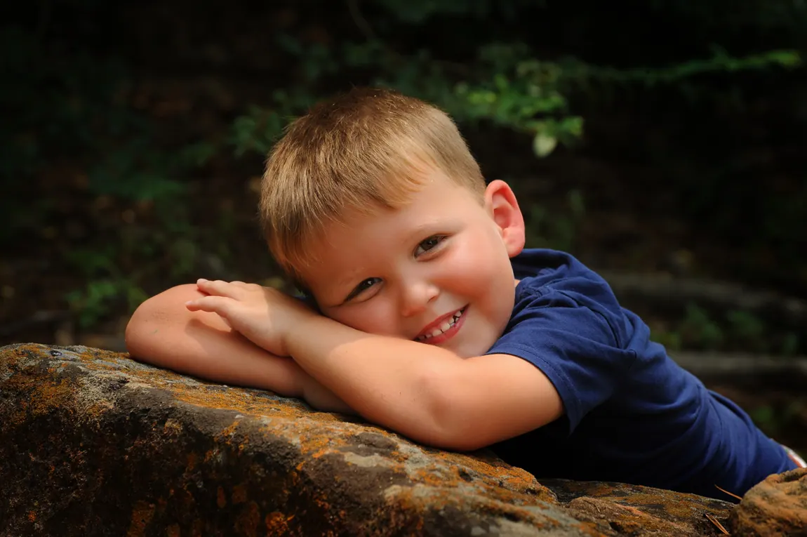 Grinning boy resting his arms on a log in the woods