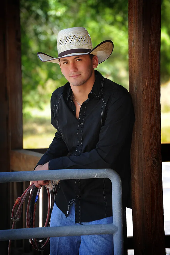 Senior in a cowboy hat holding a lariat in a covered barn
