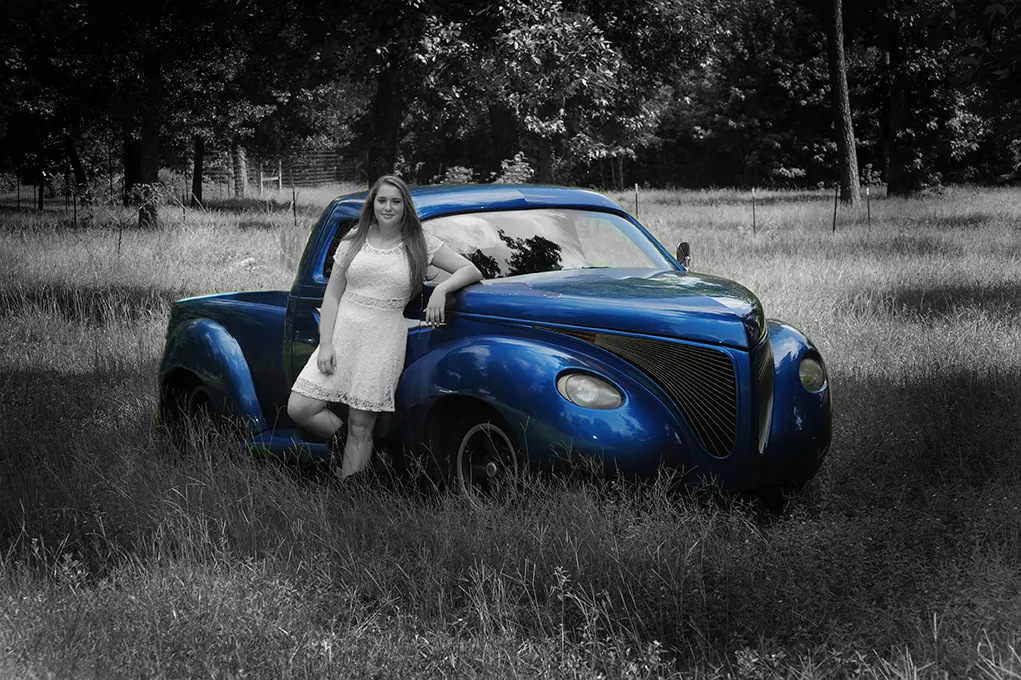 Senior girl sitting on the fender of a vintage blue truck in a field