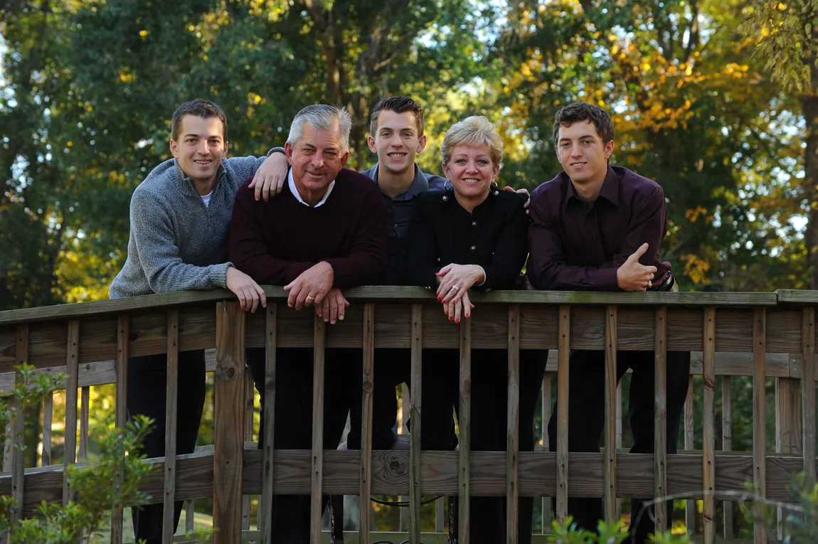 Adult family leaning on a wooden footbridge railing in the woods