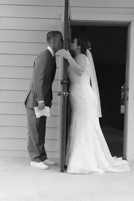 Bride and groom kissing around a door before the ceremony