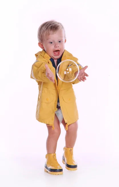 Toddler in a yellow raincoat and rain boots on a white background