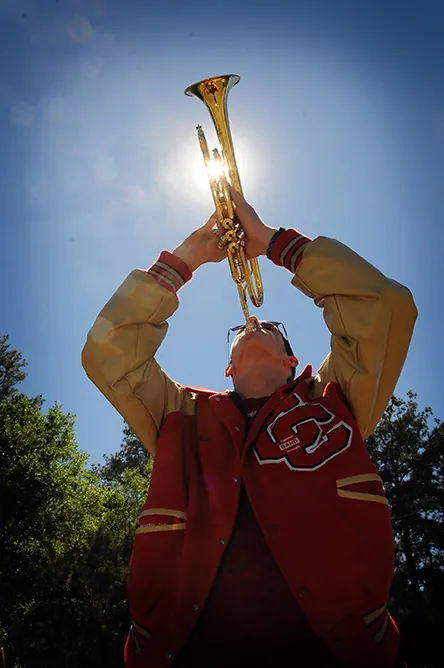 Low-angle portrait of a band senior playing trumpet toward the sun