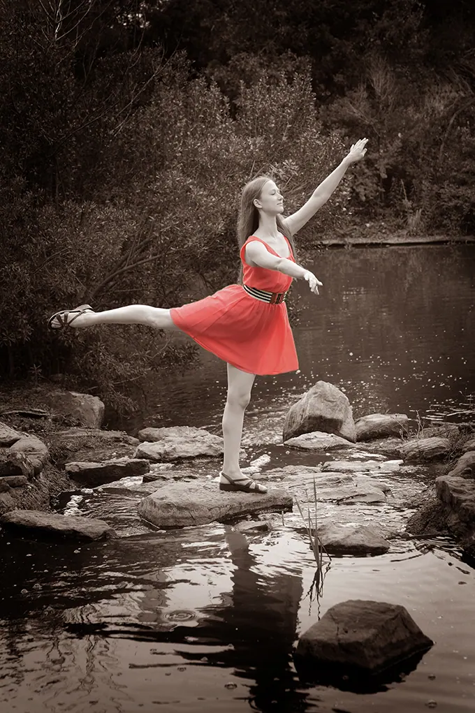Senior dancer in a red dress balancing in an arabesque on river rocks