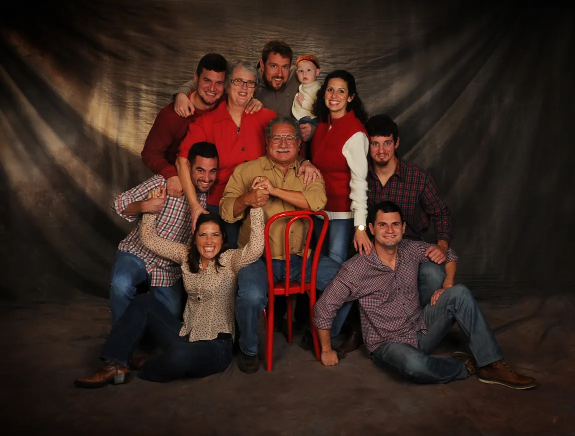 Large multigenerational family portrait with a red chair on a painted backdrop