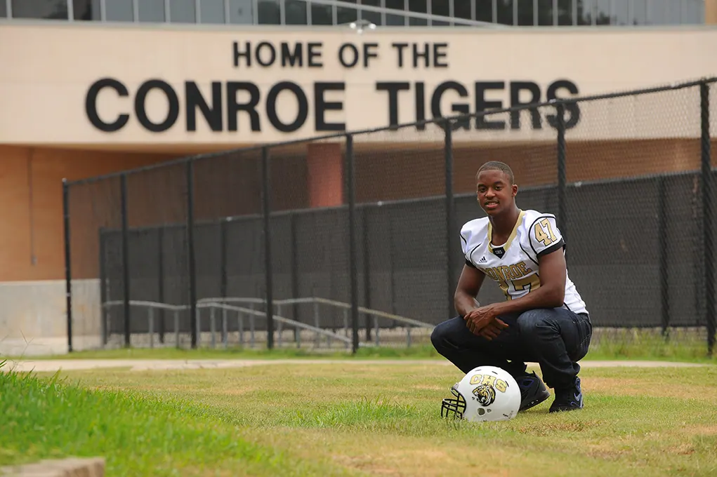 Football senior kneeling on a ball in front of the Home of the Conroe Tigers sign