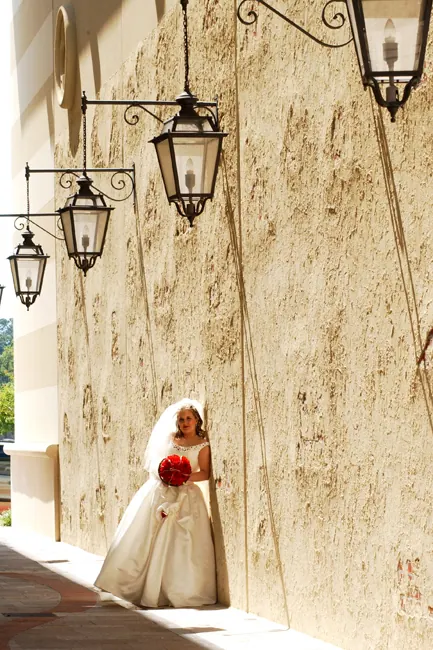 Bride holding red roses beside a stucco wall with hanging lanterns