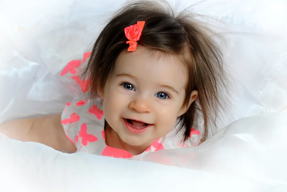 Laughing baby girl with a red bow on a white blanket