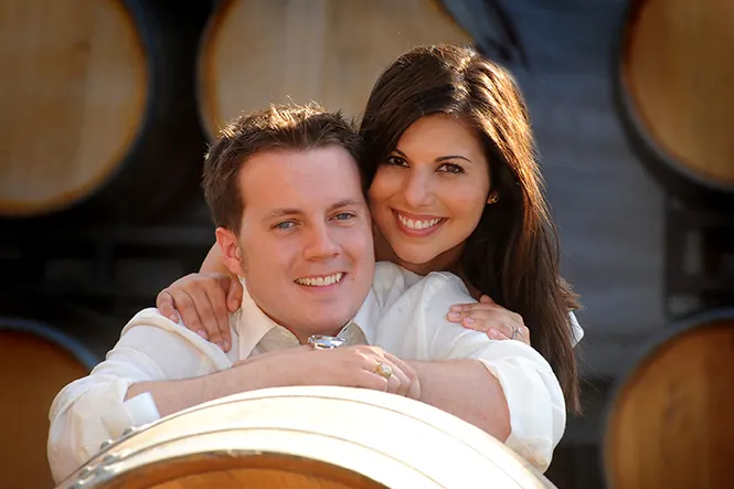 Engaged couple smiling among oak wine barrels