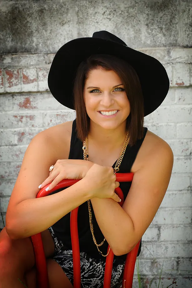 Smiling senior girl in a black hat straddling a red chair