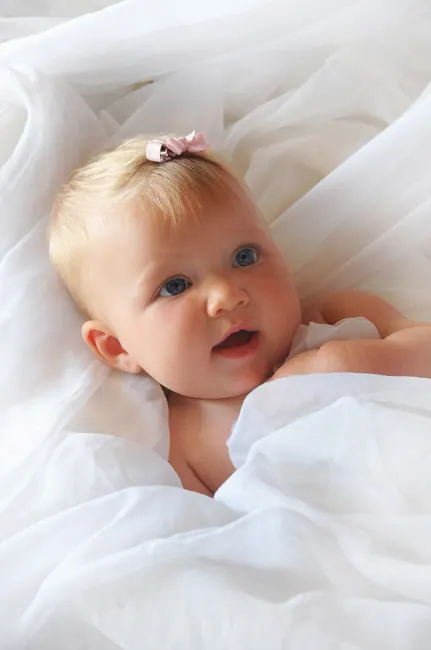 Blue-eyed baby girl with a pink clip on white fabric