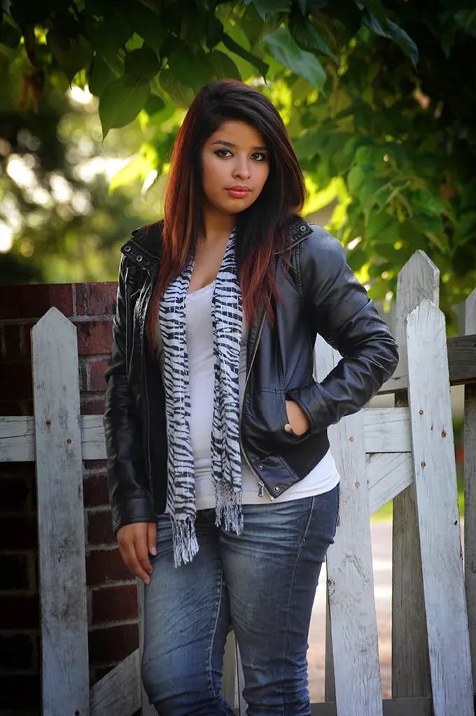 Senior girl in a leather jacket standing by a weathered white gate