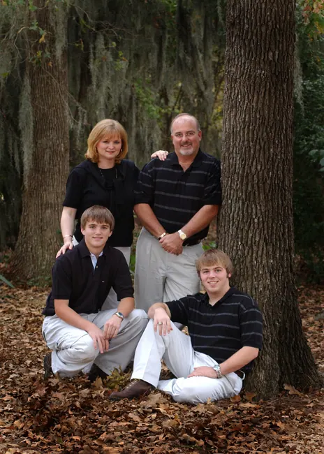 Family of four in coordinated black shirts in autumn leaves beneath a mossy oak
