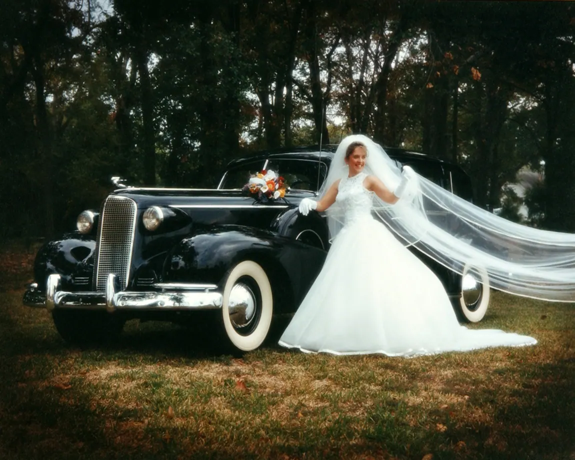 Bride with a flowing veil beside a vintage black car