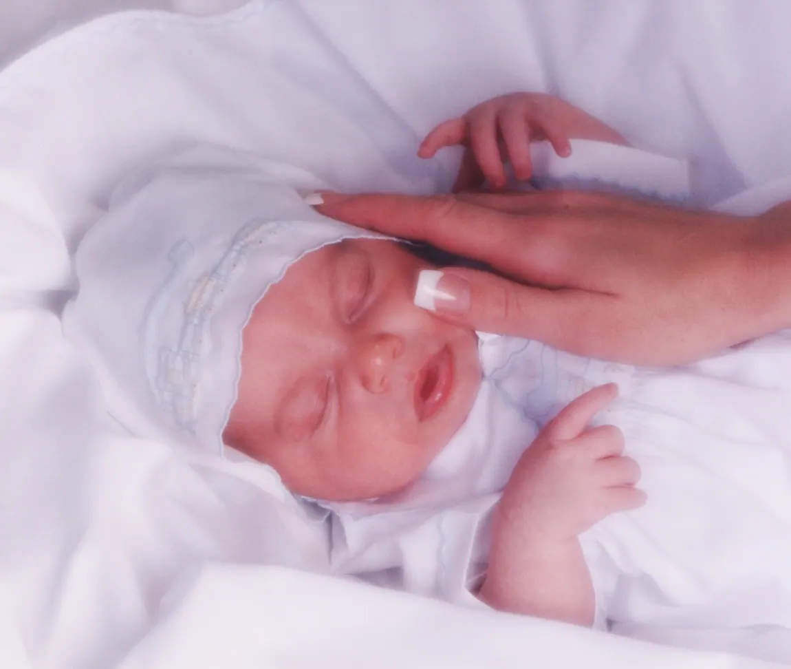 Sleeping newborn in white with a parent's hand on her head