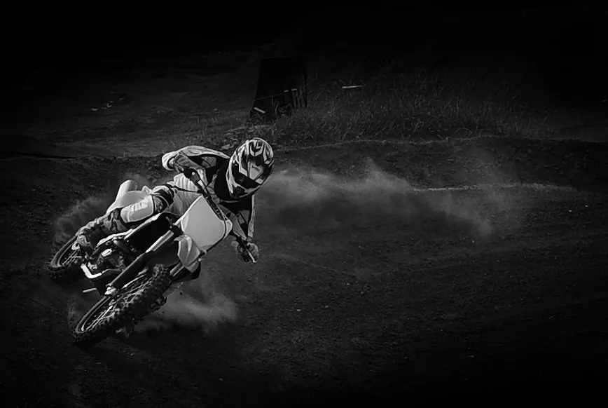 Black-and-white action portrait of a motocross rider kicking up dust through a turn
