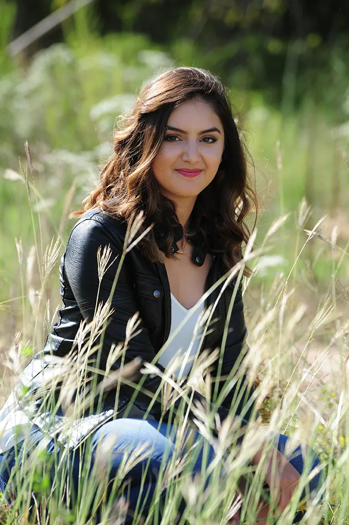 Senior girl in a leather jacket sitting in tall grass