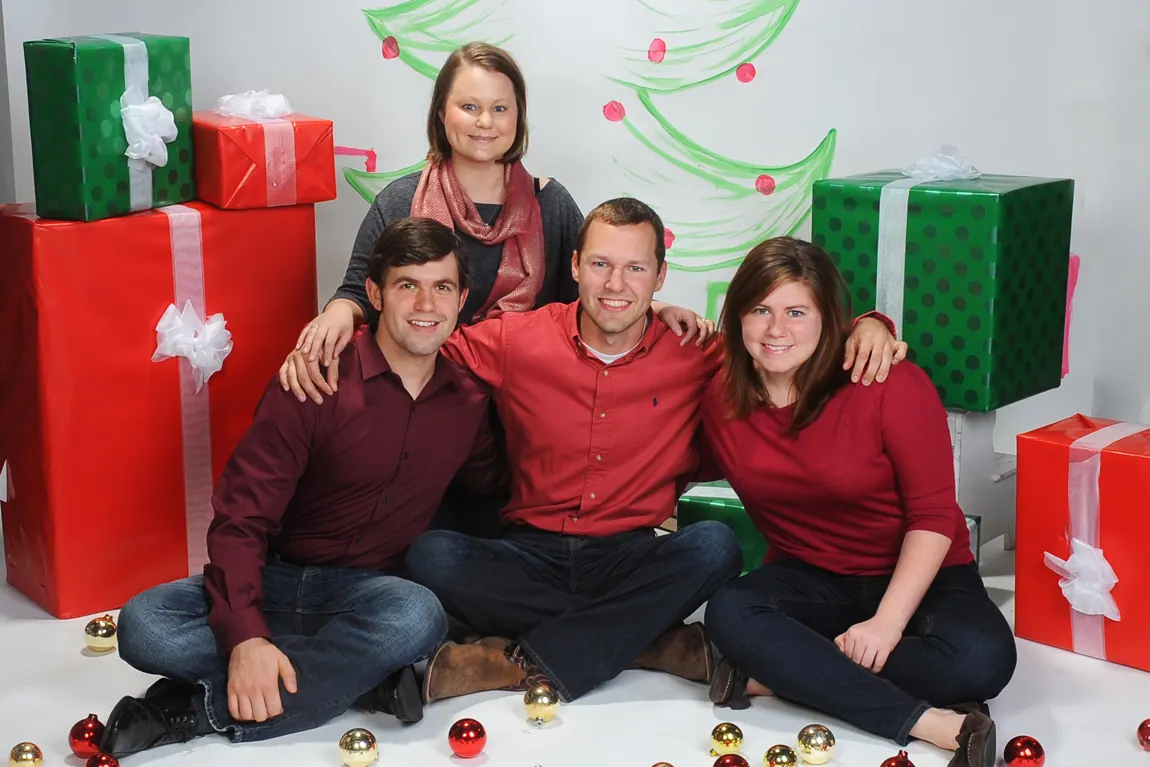 Siblings in red and black sweaters in a Christmas portrait with gift boxes
