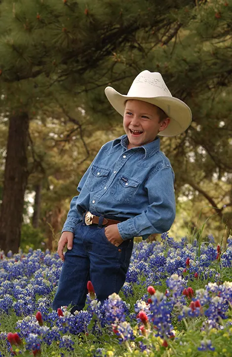 Little cowboy laughing in a field of Texas bluebonnets