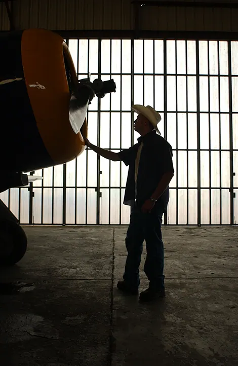 Silhouette of a senior cowboy touching a vintage airplane propeller in a hangar