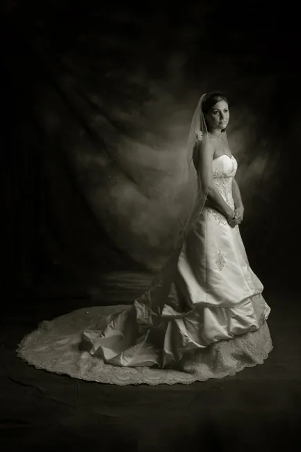 Fine-art portrait of a bride with a long lace train on a dark backdrop