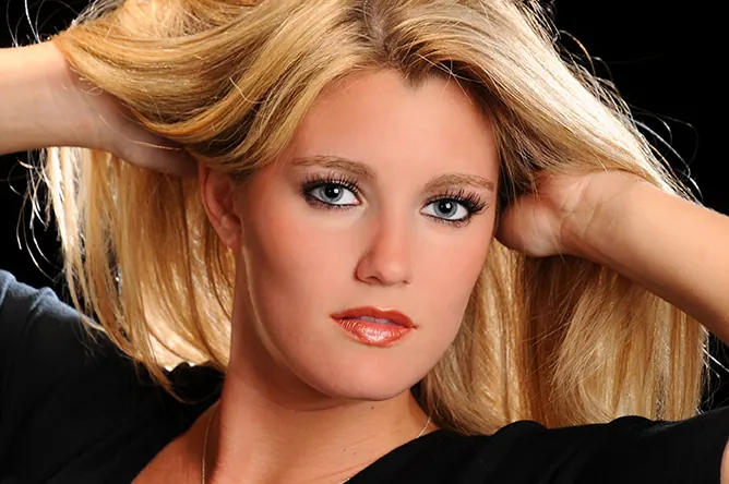 Close-up studio portrait of a blonde senior girl with her hands in her hair
