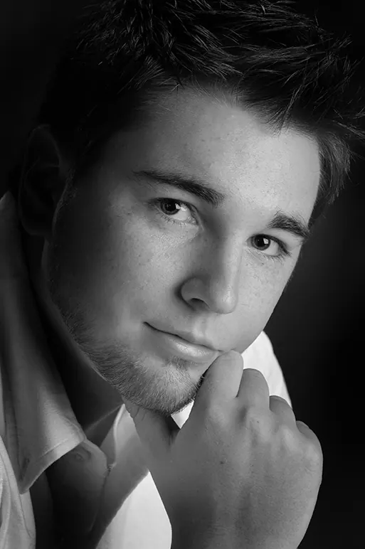 Black-and-white close-up of a senior boy resting his chin on his fist