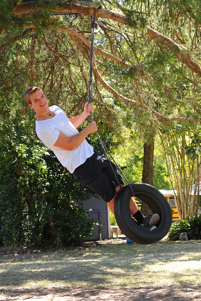 Senior boy swinging on a tire swing under a big tree