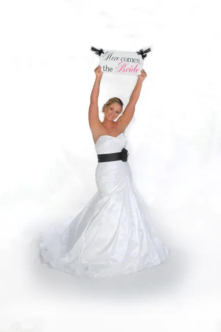 Bride holding a Here Comes the Bride sign on a white background